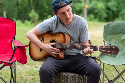 Casual young man strumming a guitar at a campsite on a summer day