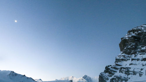 Low angle view of snowcapped mountains against clear blue sky