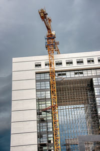 Low angle view of crane by building against sky