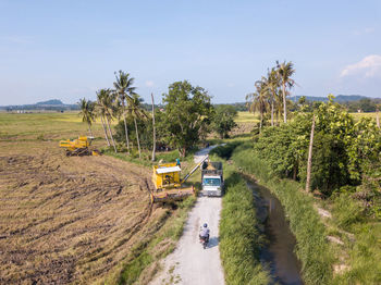 Vehicles on road amidst trees on field against sky