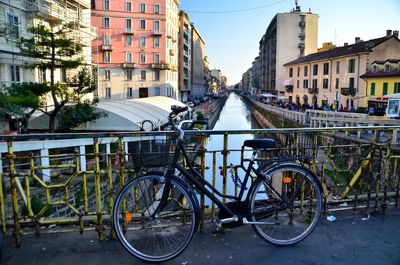 Bicycle parked on bridge over canal by buildings in city