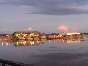 Illuminated buildings by river against sky