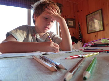 Low angle view of boy writing on book at table