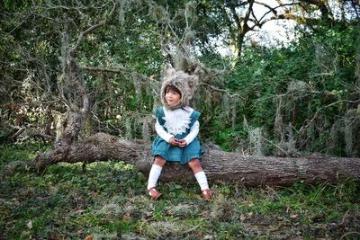 Full length portrait of girl sitting on log wearing a bear hat