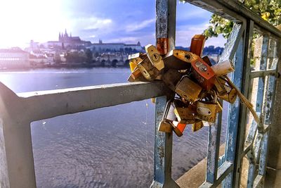 Close-up of padlocks on railing by river against sky