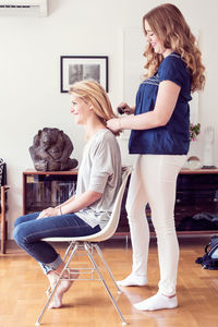 Full length side view of young woman brushing sister's hair at home