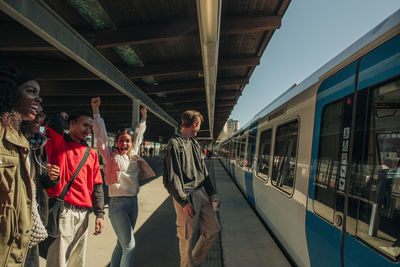 Happy multiracial friends cheering up on arrival of train at railroad station