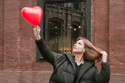 Woman holding red heart shape balloon against window