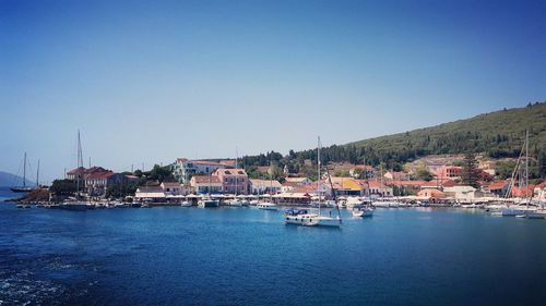 Sailboats in sea by townscape against clear blue sky