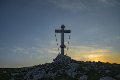 Cross on rock against sky during sunset