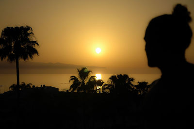 Silhouette palm trees by sea against sky during sunset