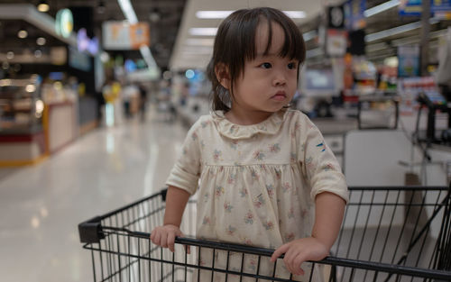 Cute girl in shopping cart at supermarket