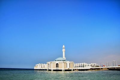 Building by sea against clear blue sky