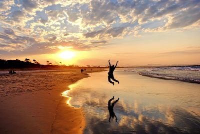 Silhouette woman jumping against sea during sunset
