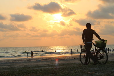 Man riding bicycle on beach against sky during sunset