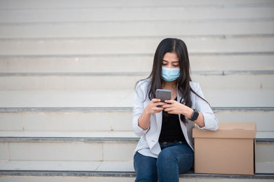 Woman using mobile phone by box on staircase