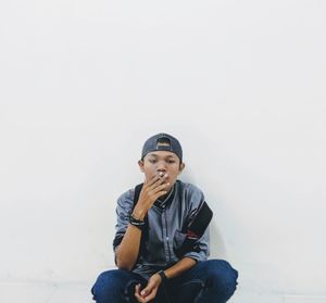 Portrait of smoker boy sitting against white wall 