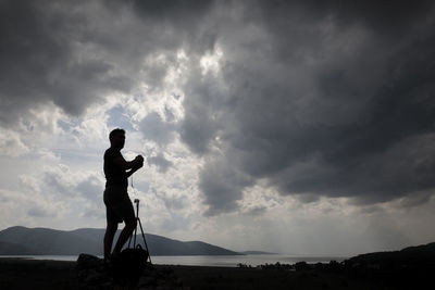 Silhouette man standing on shore against sky