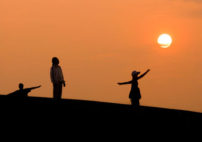 People standing by scarecrow against orange sky