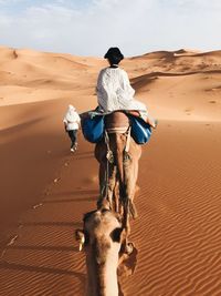 Rear view of woman riding camel at desert