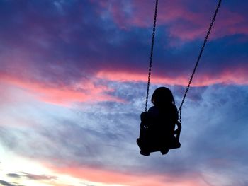 Low angle view of silhouette child enjoying swing against sky during sunset