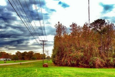 Electricity pylon on field against cloudy sky