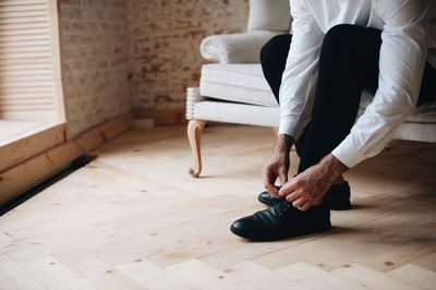 Low section of man tying shoelace on sofa at home