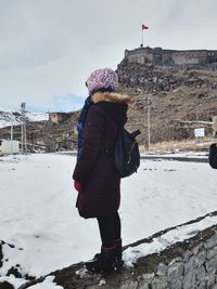 Rear view of woman standing on snow covered field against sky