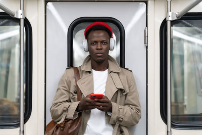 Black man in subway train using smartphone listens to music with headphones in public transportation