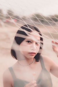 Portrait of beautiful woman holding lollipop standing by net