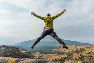 Rear view of man jumping on cliff against landscape