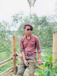 Young man wearing sunglasses standing against trees