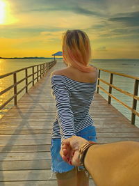 Woman holding cropped hand while standing on pier over sea