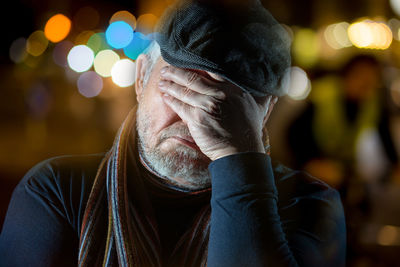 An older man is sitting outside at night. he is tired, rests his head on one hand and sleeps. 