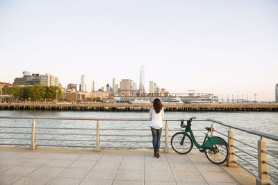 Rear view of woman with bicycle looking at city view while standing on observation point