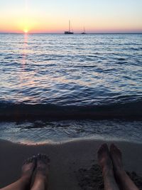 Low section of person on beach against sky during sunset