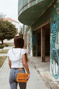 Rear view of woman walking on footpath against building