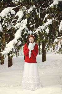 Redhead beautiful woman in red sweater and white gloves walking in the frozen winter forest.