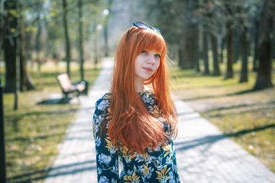 Portrait of young woman standing by tree in park
