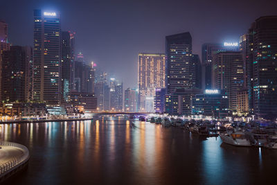 Illuminated city by river against sky at night