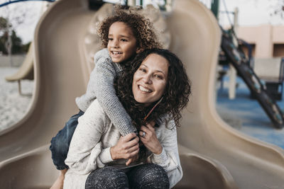 Son hugging happy mother on slide outside at park playground at dusk