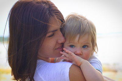 Close-up of mother carrying cute daughter against sky