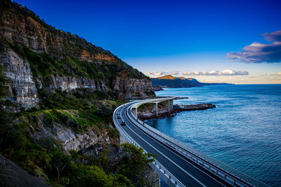 Scenic view of mountain by sea against blue sky