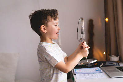 Boy pronouncing sound o looking at mirror doing an online speech therapy lesson through a laptop