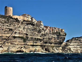 Sea by cliff against clear blue sky