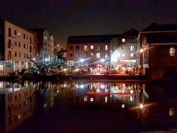 Illuminated buildings by canal against sky at night