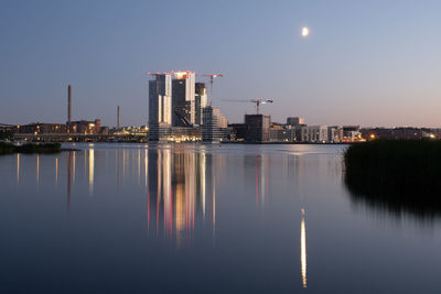 Reflection of illuminated buildings in lake against sky at night