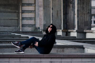 Side view of woman wearing sunglasses while sitting below bridge