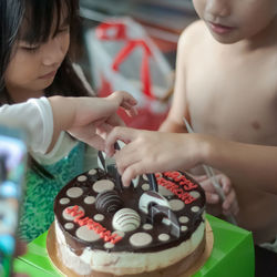 Midsection of shirtless boy decorating cake with sister