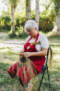 Mature artisan weaving esparto grass in garden